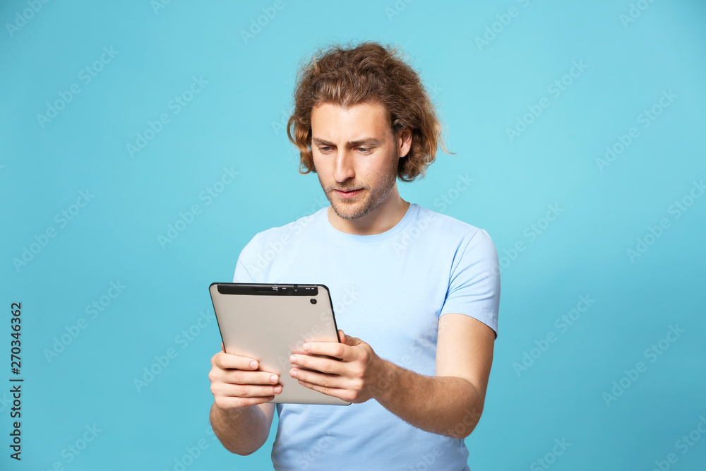 Handsome man with tablet computer on color background