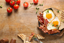 Frying Pan With Tasty Eggs, Bacon And Toasts On Table