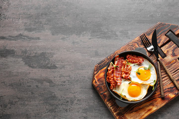 frying pan with tasty eggs and bacon on grey background