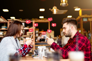 Attractive Caucasian couple dressed casual using smart phones for social media while sitting in cafe.