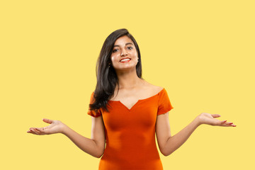 Beautiful female half-length portrait isolated on yellow studio background. Young emotional indian woman in dress pointing and showing. Negative space. Facial expression, human emotions concept.