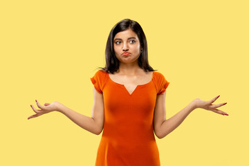 Beautiful female half-length portrait isolated on yellow studio background. Young emotional indian woman in dress doubts and can't choose. Negative space. Facial expression, human emotions concept.