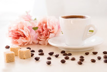 Breakfast In Pastel Colors. Cup Of Coffee Standing On The Table With Coffee Beans Scattered Around And Pieces Of  Cane Sugar , Against The Window And Flowers