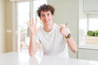 © Krakenimages.com - Young handsome man wearing white t-shirt at home showing and pointing up with fingers number seven while smiling confident and happy.
