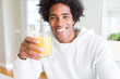 African American man holding and drinking glass of orange juice with a happy face standing and smiling with a confident smile showing teeth