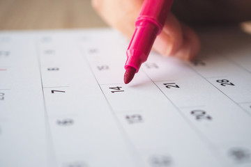 Hand with pen writing on calendar page closeup