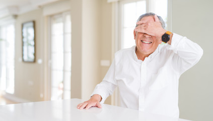 Sticker - Handsome senior man at home smiling and laughing with hand on face covering eyes for surprise. Blind concept.