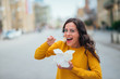 © bnenin - Cheerful young woman eating food from takeaway box in the city, looking at camera, copy space.