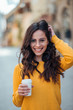 © bnenin - Happy young brunette woman with takeout coffee in urban background, smiling at camera.