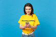 © ViDi Studio - Portrait of smiling beautiful young woman in vivid casual clothes using mobile phone typing sms message isolated on bright blue wall background in studio. People lifestyle concept. Mock up copy space.