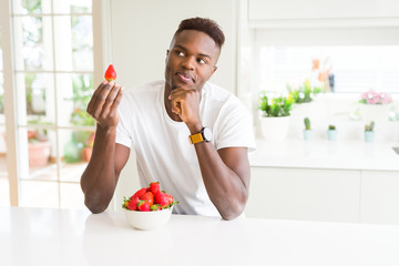 Canvas Print - African american man eating fresh healthy strawberries serious face thinking about question, very confused idea