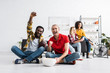 © LIGHTFIELD STUDIOS - Happy and positive multicultural young people sitting on floor and watching sport game with bowl of popcorn