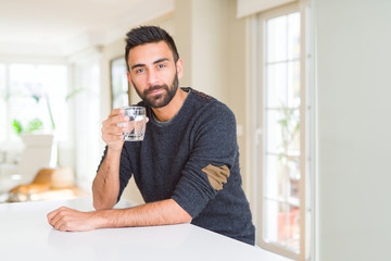 Handsome hispanic man drinking a fresh glass of water with a confident expression on smart face thinking serious