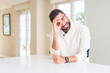 © Krakenimages.com - Handsome hispanic man wearing casual white sweater at home doing ok gesture with hand smiling, eye looking through fingers with happy face.