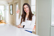 © Krakenimages.com - Beautiful young woman sitting on white table at home pointing finger up with successful idea. Exited and happy. Number one.