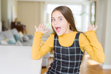 Wall Mural - Beautiful young girl kid sitting on the table celebrating crazy and amazed for success with arms raised and open eyes screaming excited. Winner concept