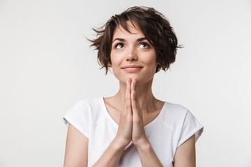 Canvas Print - Portrait of european woman with short brown hair in basic t-shirt keeping palms together and praying