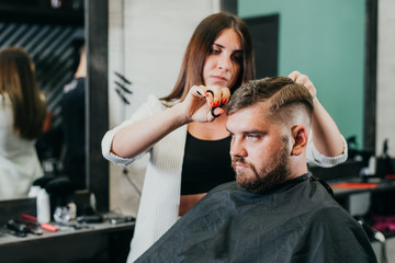 Canvas Print - the barber cuts a bearded man with scissors in the salon