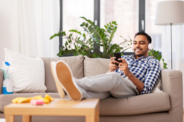 Sticker - people, housework and housekeeping concept - indian man in headphones listening to music on smartphone after home cleaning