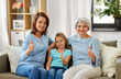 © Syda Productions - family, generation and female concept - portrait of smiling mother, daughter and grandmother sitting on sofa and showing thumbs up at home