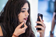 young woman, touching up makeup with smartphone camera