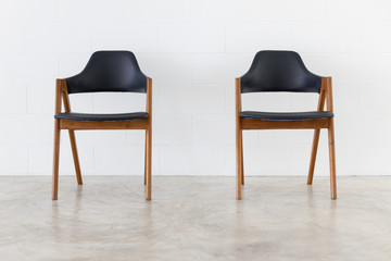 Wall Mural - front view of two wooden leather chair on white concrete wall background.