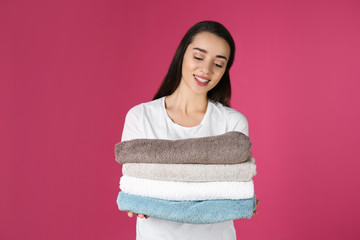 Poster - Happy young woman holding clean towels on color background. Laundry day