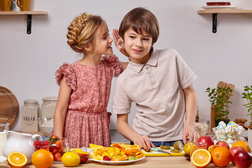 Cute kids are cooking together in a kitchen against a white wall with shelves on it.