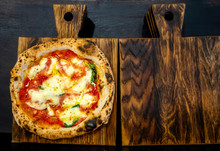 Neapolitan Pizza On A Dark Wooden Chopping Board. Top View, Macro, Black Background