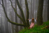 Fototapeta Zwierzęta - Woman lost in the woods. Red head woman in foggy forest near the tree covered with moss. Spring rainforest in Columbia River Gorge near Portland. Oregon. United States of America.