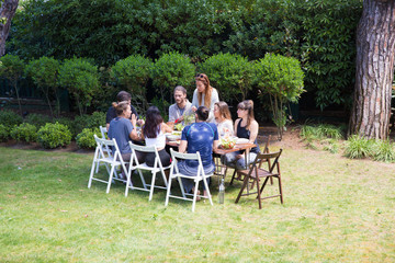 Wall Mural - Group of young people sitting in garden having meal. Family or friends resting at garden party. Outdoor party concept