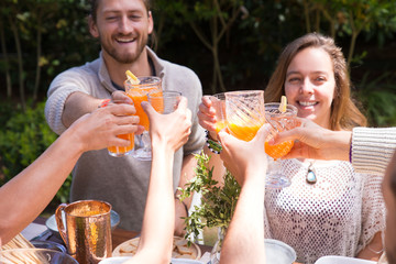 Portrait of happy young friends toasting juice outdoors. Man and woman having lunch with friends outside. Outdoor party concept