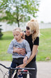 © supersomik - Happy family in the summer park. Mother teaches her daughter to ride a bicycle in the park