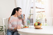 © Paul - Beautiful brunette woman sitting at dining table eating a healthy salad and drinking coffee or tea with a bowl of fruits on table with garden in the background