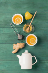 Wall Mural - Tea lemon ginger honey in a white cup and a teapot on a wooden background. Healthy drink for detox health. Flat layout