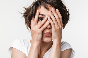 Portrait of cute woman with short brown hair in basic t-shirt covering her eyes with hands