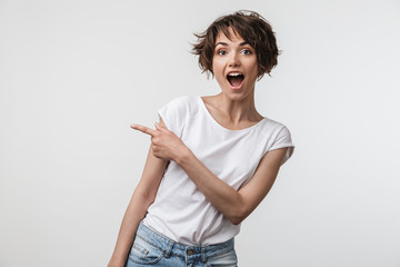 Wall Mural - Portrait of brunette woman with short hair in basic t-shirt rejoicing and pointing finger at copyspace