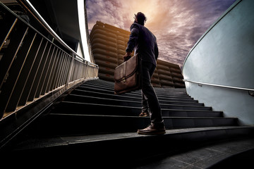 Young businessmen have power of ambition to work on the morning. He confidently stepped up the stairs. In his hand holding a business leather bag.