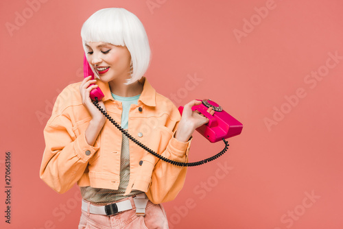 Plakat smiling girl in white wig talking on retro telephone, isolated on pink