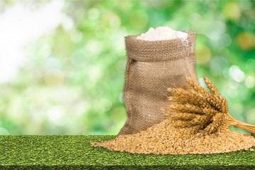 Wall Mural - Wheat ears and flour on wooden desk on blurred field background