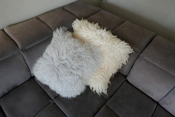 Two cuddly lambskin pillows on a gray velor sofa, close-up