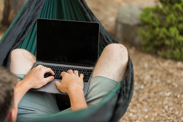 Man working on laptop in hammock in forest