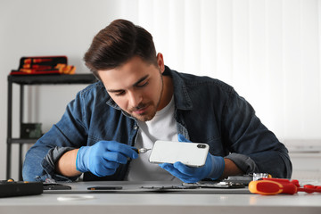 Wall Mural - Technician repairing broken smartphone at table in workshop