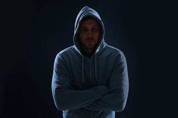 Wall Mural - Mysterious man in hoodie on dark background. Dangerous criminal