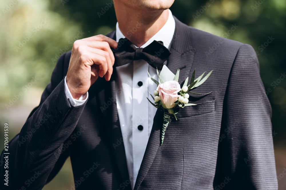 the groom in a suit straightens his tie bubochku. boutonniere on the lapel of his jacket. young man in a business suit.