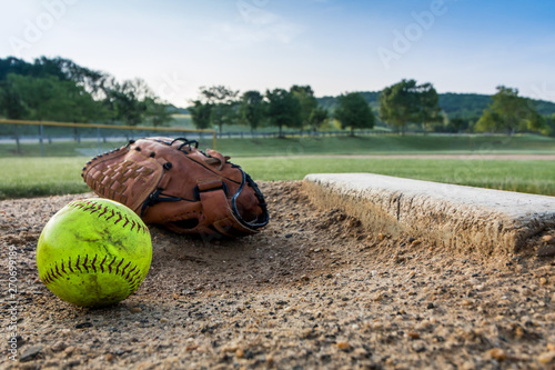 Worn softball and glove on pitchers mound on early morning springtime
