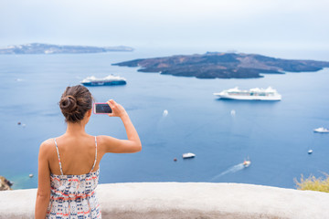 Fototapete - Europe cruise vacation summer travel tourist woman taking picture with phone of Mediterranean Sea in Santorini, Oia, Greece, with cruise ships sailing in ocean background.