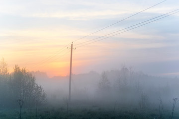 Power transmission line supporting structure at sunrise in the fog