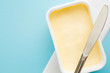 Opened plastic pack of light yellow margarine and knife. Closeup. Empty place for text or logo on pastel blue desk.