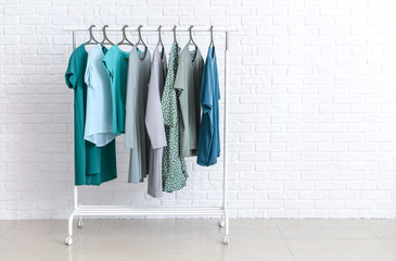 Rack with clothes after dry-cleaning near white brick wall